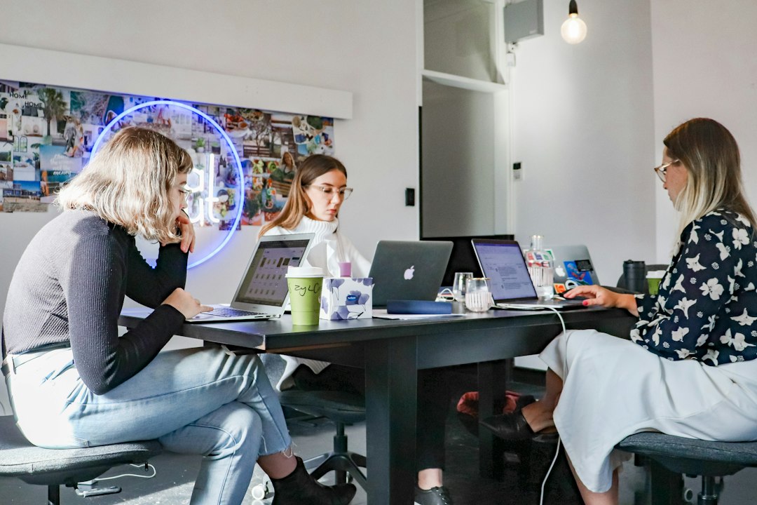 3 women sitting on chair in front of table with laptop computers marketing team laptops brand mentions