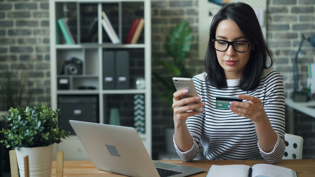 a woman sitting at a table looking at her cell phone instant payments bank transfer small business finance