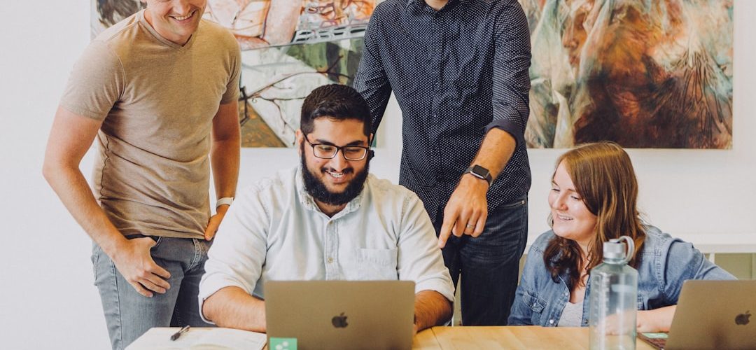 four coworkers smiling around laptop at table team reviewing funnel optimization meeting data insights