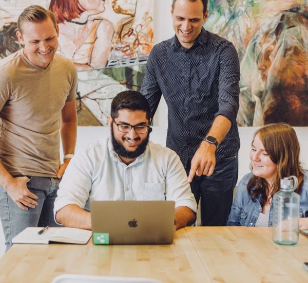 Kopify Review: Content Writing Quality, Pricing, and Turnaround Times 3 four coworkers smiling around laptop at table team reviewing funnel optimization meeting data insights