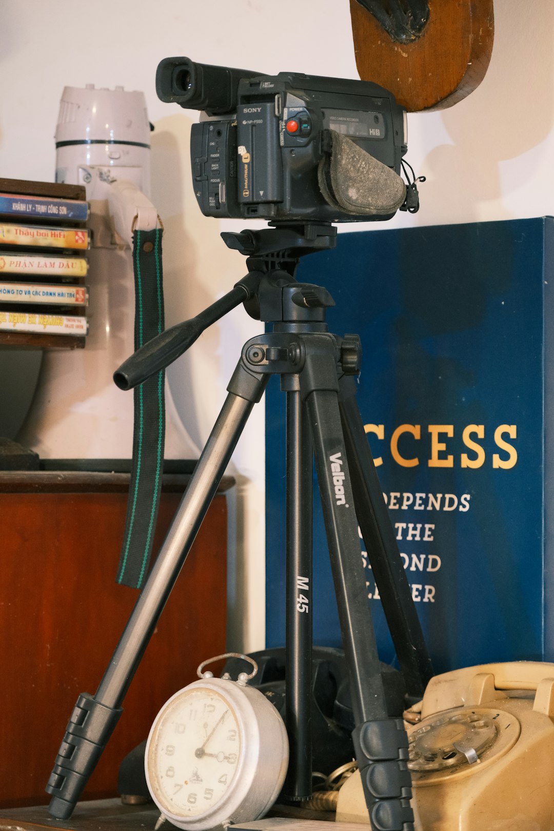 a camera on a tripod in front of a book tripod camera microphone video gear desk setup