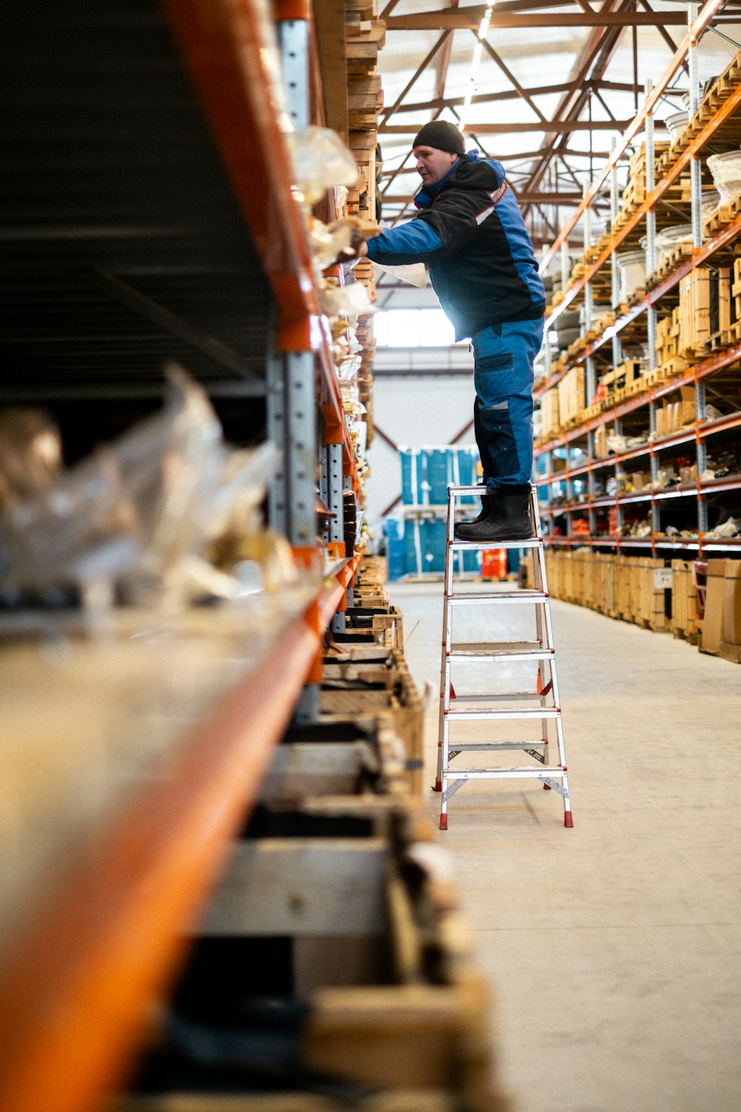 a man standing on a ladder in a warehouse phone scanner inventory shelves barcode app