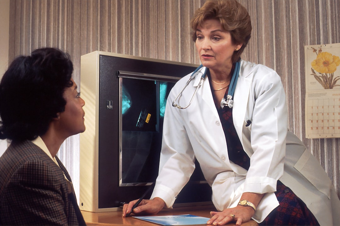 doctor sitting on desk talking to sitting woman video interpreter screen patient care clinical consultation