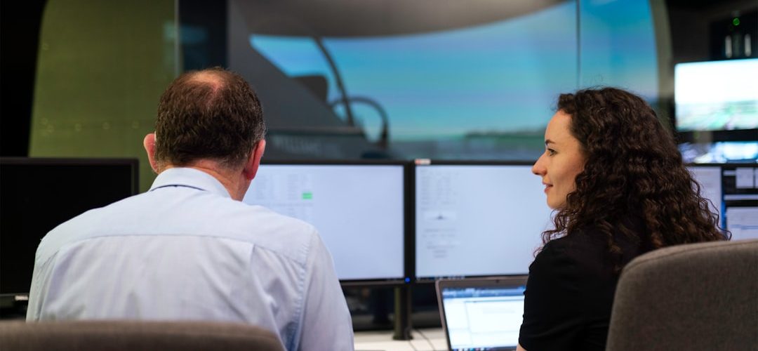 man in white dress shirt sitting beside woman in black shirt technology newsroom digital innovation data screens