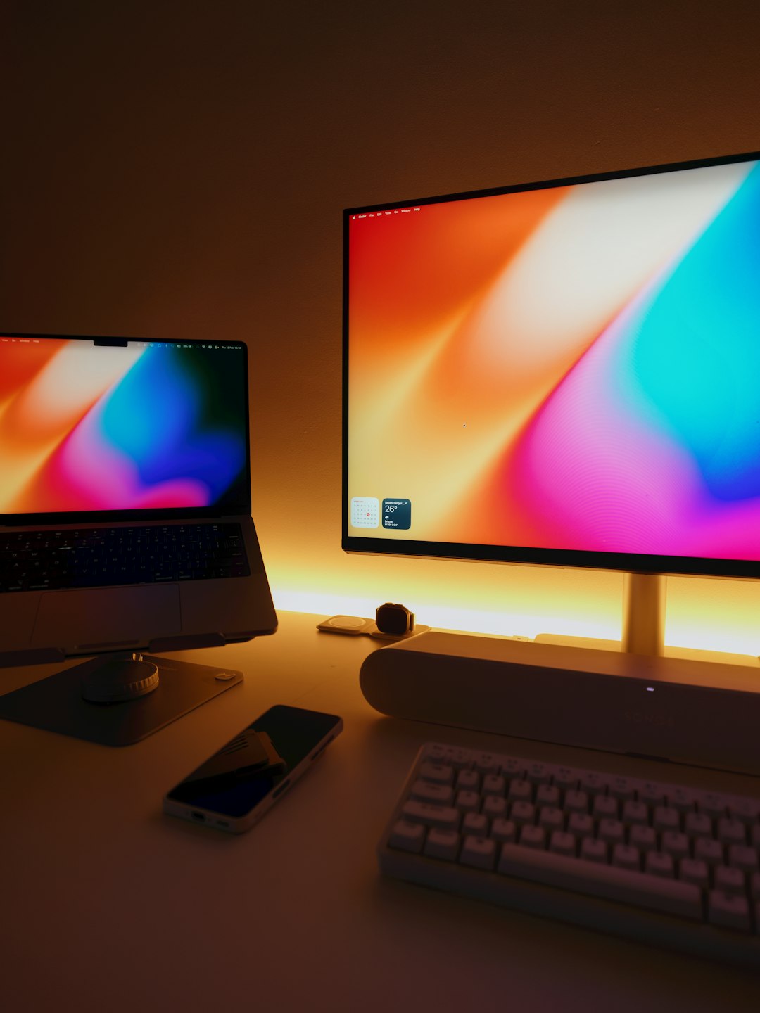 modern desktop setup with laptop and monitor macbook startup screen waveform audio editing creative workspace