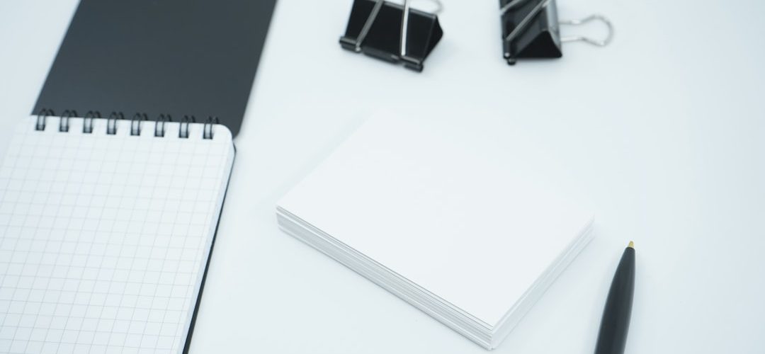 white and black notebook beside black pen business cards color swatches office desk