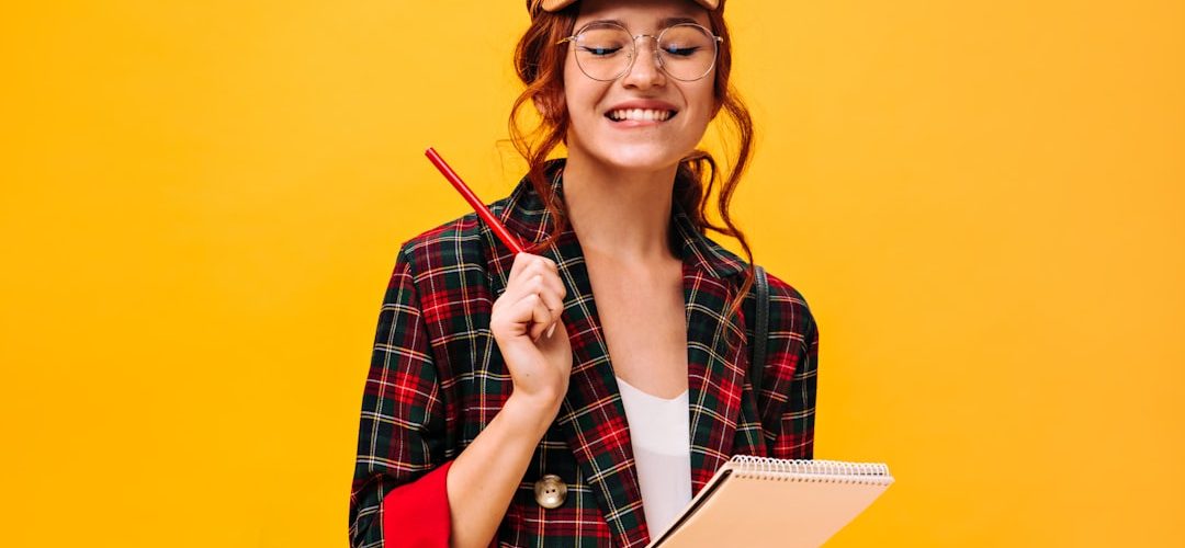 a woman in a plaid jacket holding a pen and notebook study notes quiz checklist smiling student
