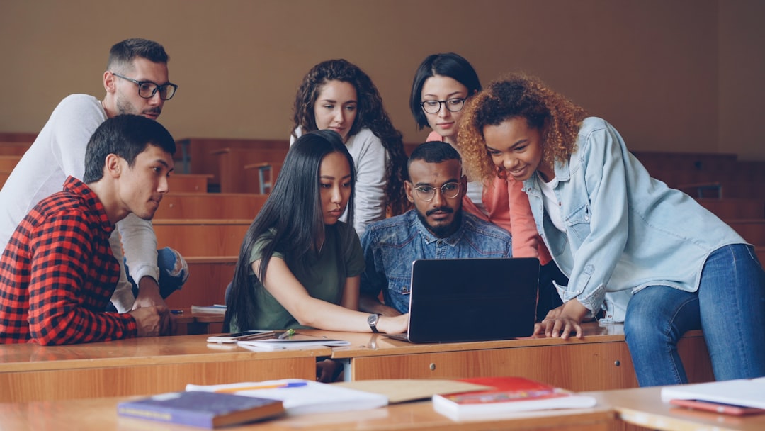 diverse group of students gathered around laptop students campus timetable planning college technology