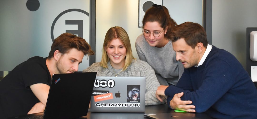 four people collaborating around a laptop on a table in a modern office team collaboration video production online workflow