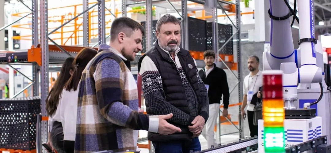 men observe automated conveyor belt system in warehouse industrial 3d printing engineered parts manufacturing facility