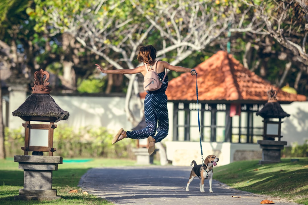 woman in black and white polka dot tank top and black and white pants jumping on near near near near happy couple dog engagement sign park