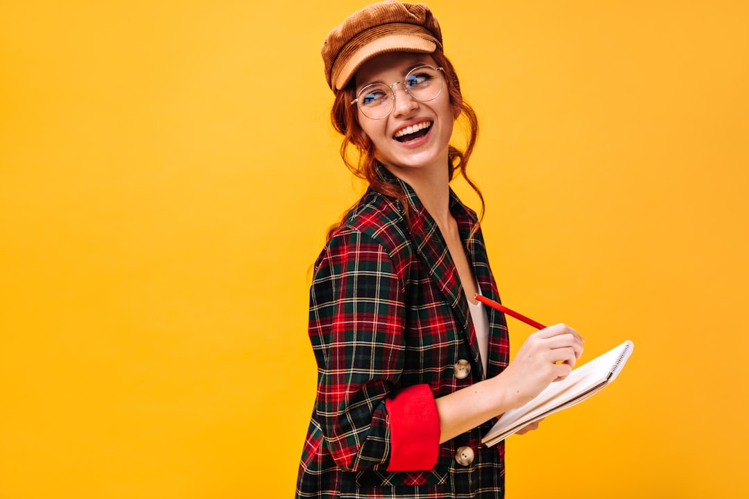a woman wearing glasses and a hat holding a book study notes quiz checklist smiling student