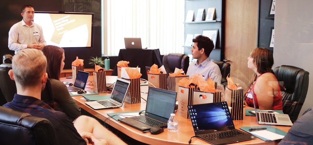 man standing in front of people sitting beside table with laptop computers leadership discussion planning session progress charts collaboration 1