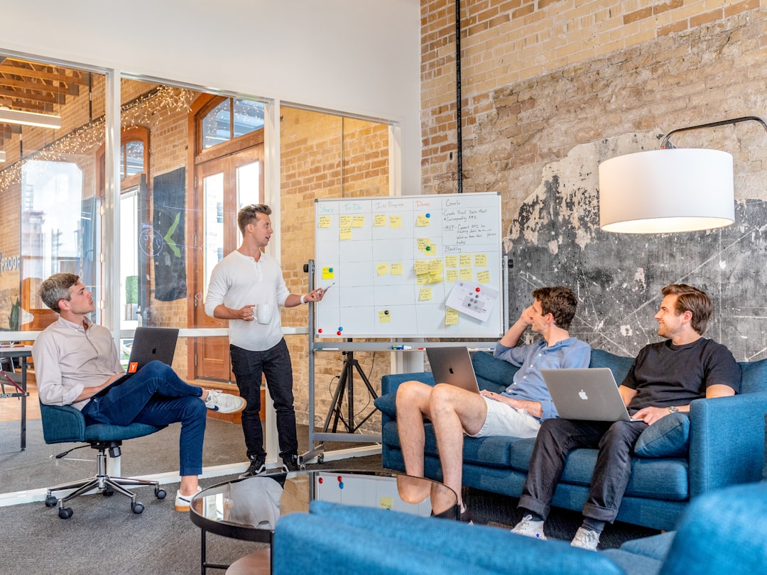three men sitting while using laptops and watching man beside whiteboard company meeting team presentation office audience