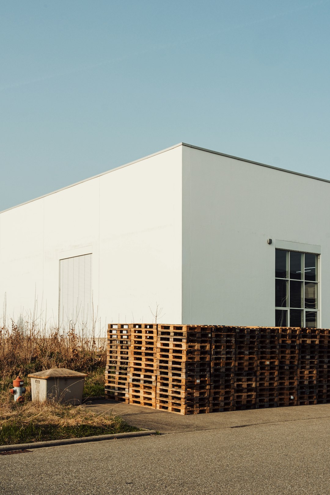 white building with stacked wooden pallets outside warehouse pallets boxed merchandise wholesale inventory
