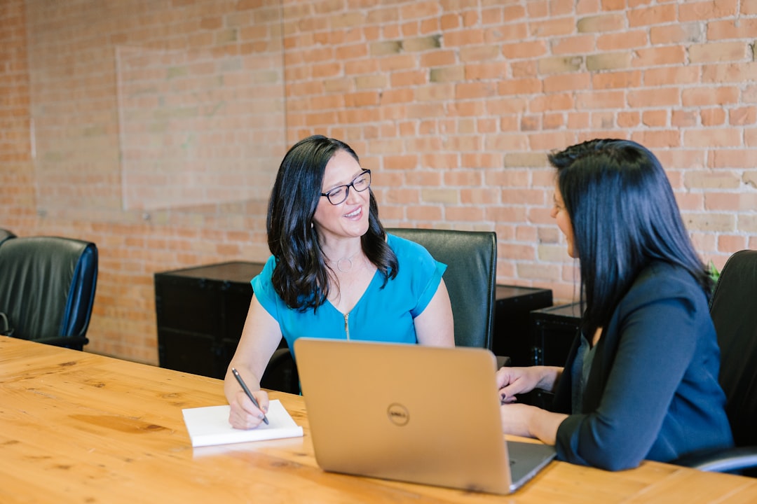 woman in teal t shirt sitting beside woman in suit jacket employee questions meeting discussion open communication