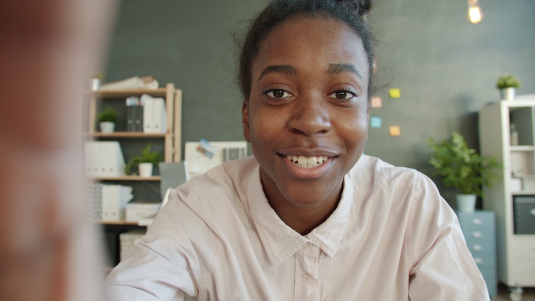 young woman smiles at the camera in an office setting remote team video call virtual workspace