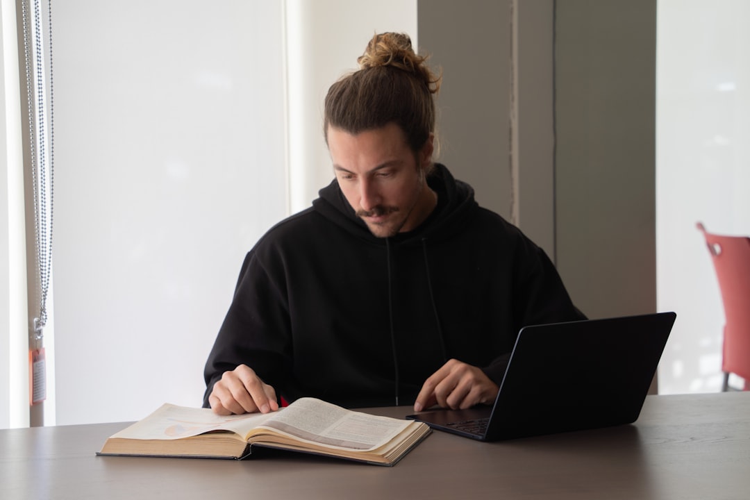 man reads a book while using his laptop student laptop language notes vocabulary practice