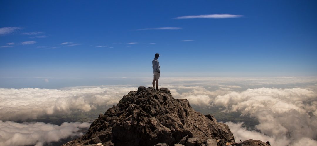 man standing on top of rock formation mountain summit ambitious team future vision