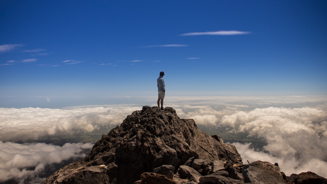 man standing on top of rock formation mountain summit ambitious team future vision