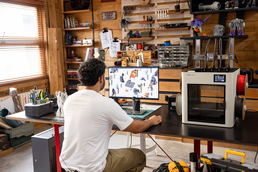 man working on computer in a workshop with 3d printer cad software comparison laptop design engineering tools 3d models