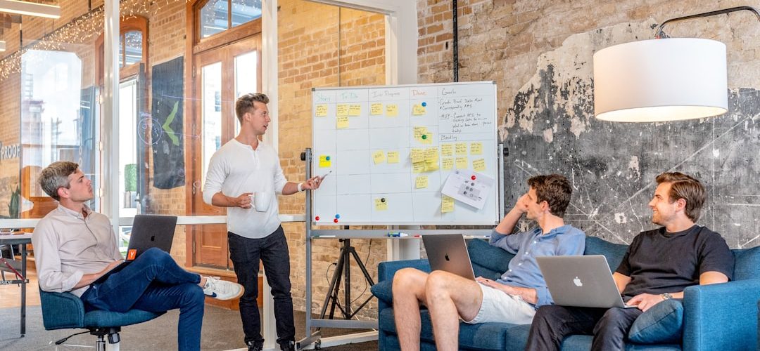 three men sitting while using laptops and watching man beside whiteboard case workflow automation team collaboration