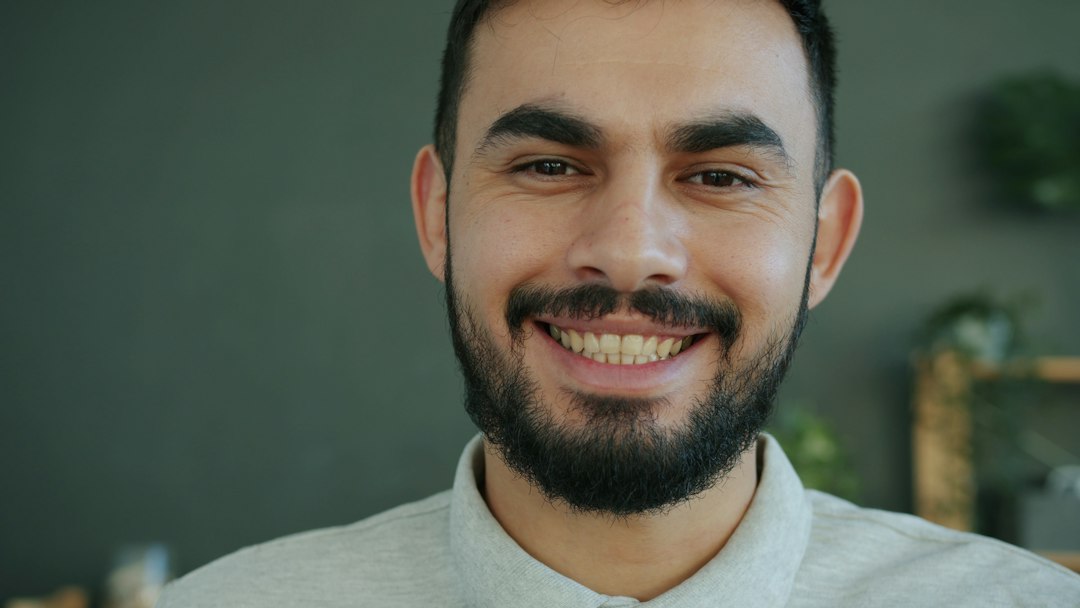 a smiling man with a beard wearing a collared shirt host greeting guests travel welcome front door warm smile