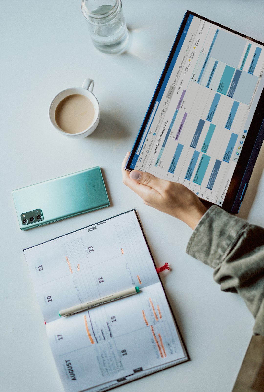 person holding ipad near white ceramic mug and laptop content calendar social reports marketing team