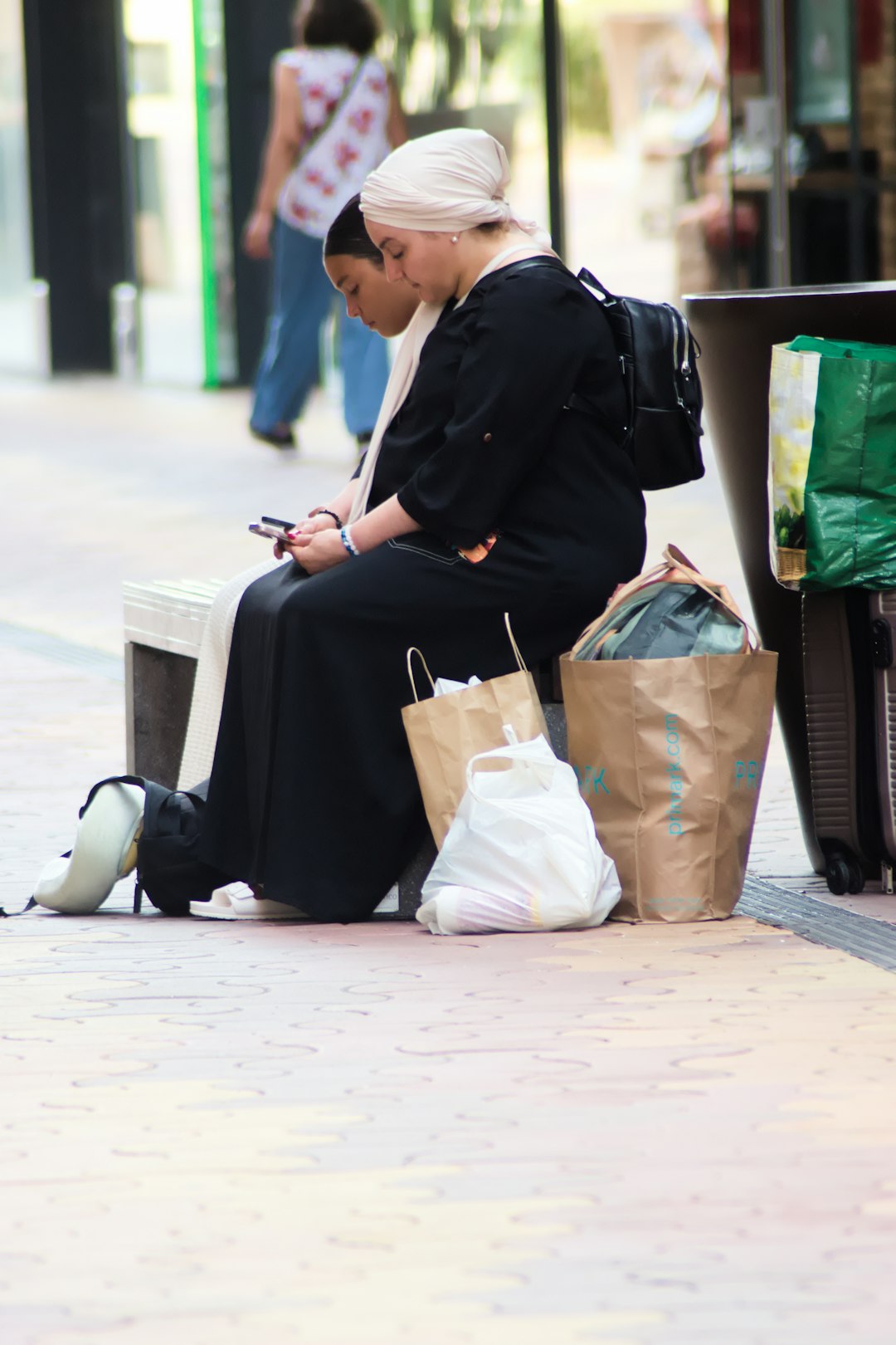 two people in black clothing sitting on a bench with shopping bags ramadan evening mobile shopping family iftar