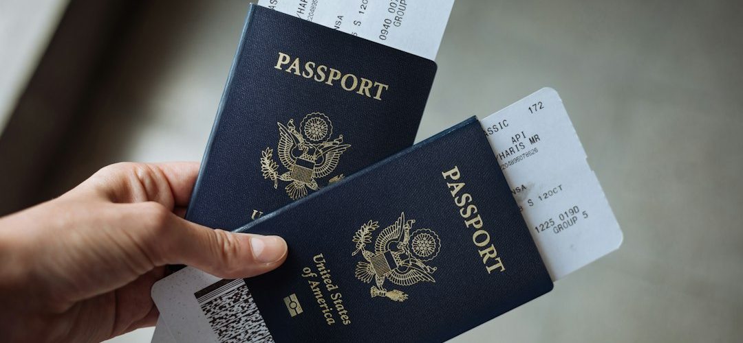 a hand holding two united states passports with airline boarding passes tucked inside immigration form work permit application documents
