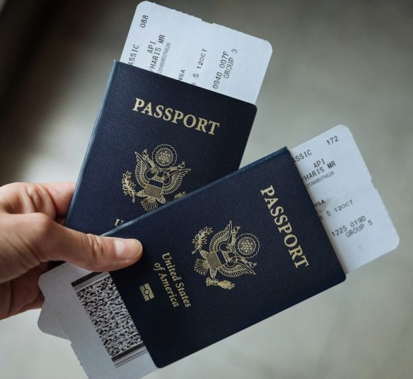 a hand holding two united states passports with airline boarding passes tucked inside immigration form work permit application documents