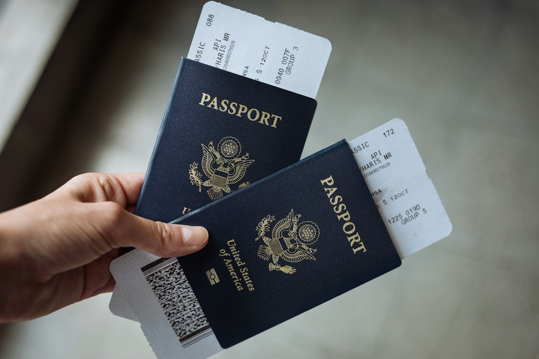 a hand holding two united states passports with airline boarding passes tucked inside immigration form work permit application documents